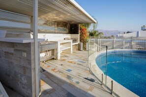 A poolside area with a built-in barbecue, a seating area, and a view of mountains.