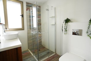 A modern bathroom with a glass-enclosed shower, a white sink, and a wooden vanity.