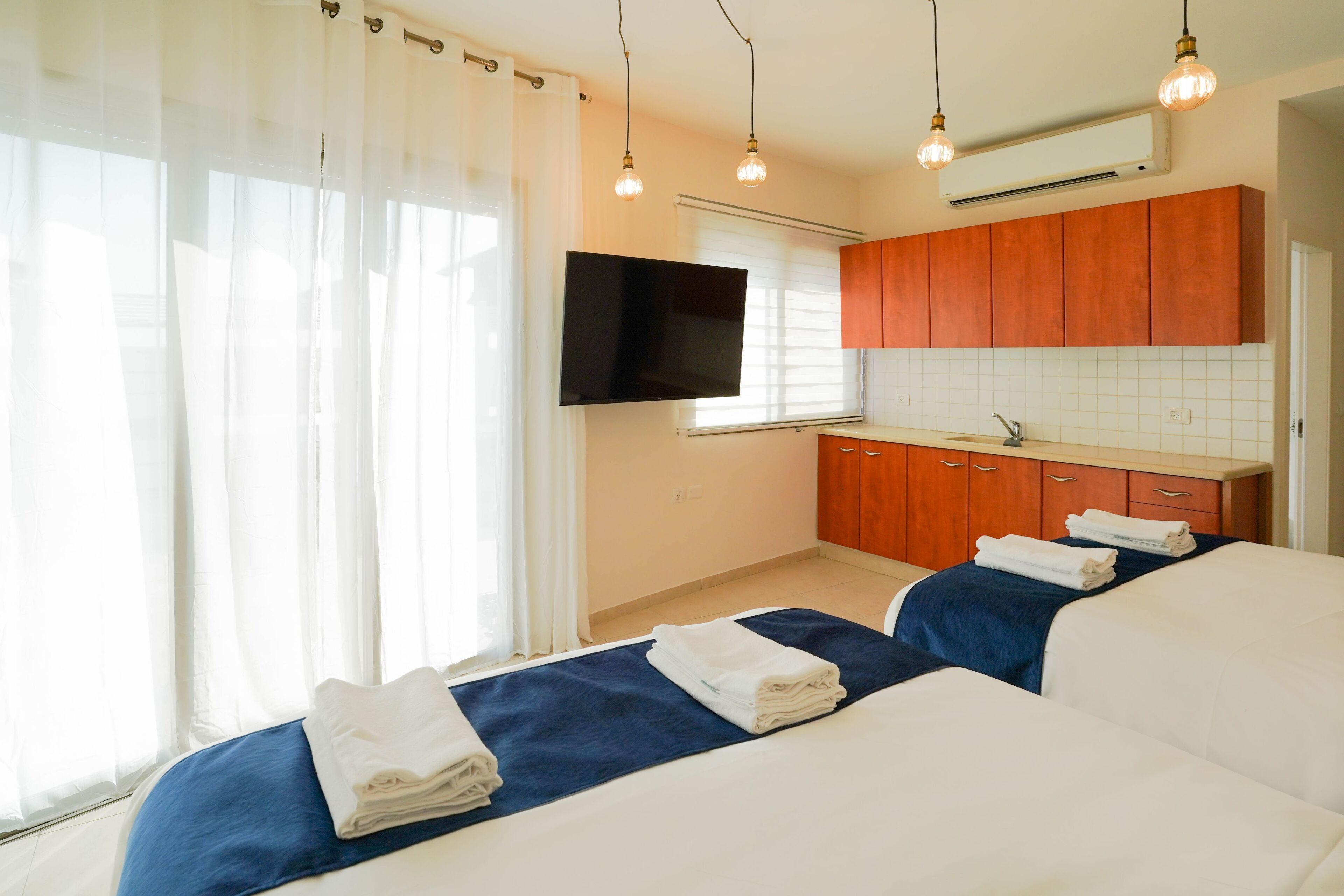 Habitación de hotel con dos camas, televisión, kitchenette y un amplio ventanal con cortinas.