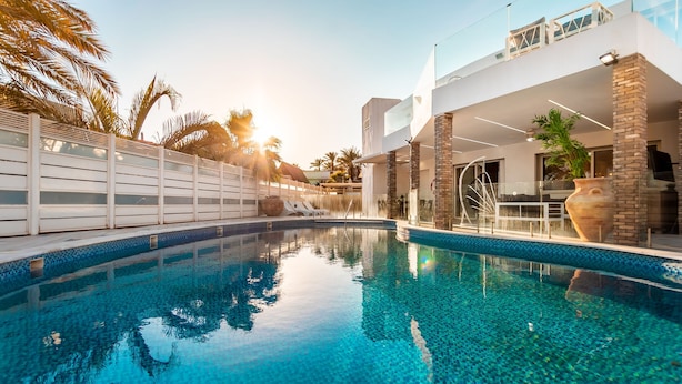 Ein moderner Poolbereich mit klarem, blauem Wasser, einem weißen Zaun und einem zweistöckigen Gebäude mit Balkon.