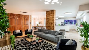 Ein modernes Wohnzimmer mit einem grauen Sofa, schwarzen Sessel und einem Couchtisch. Im Hintergrund steht ein Holzschrank und ein großes Aquarium.