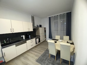 Una cocina moderna con armarios blancos, encimera negra y una zona de comedor con mesa y sillas.