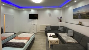 A modern living room with a sofa, two beds, a TV, and a painting on the wall. - Schöne Wohnung 72qm, Nähe Stadt- & Schulzentrum, 8 km von der Tschechei Entfernt (Selb)