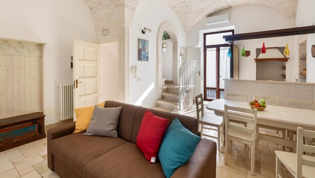 A cozy living room with a brown sofa, a dining table with chairs, and a staircase leading to an upper floor. - 3189 Dimora Bellargo by Barbarhouse (Martina Franca)