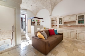 A spacious living area with a brown sofa, a kitchen with white cabinets, and a staircase leading to another level.