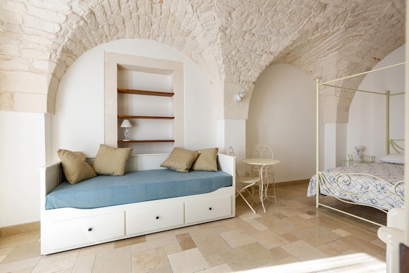 A bedroom with a built-in sofa bed, a small table, and a four-poster bed.