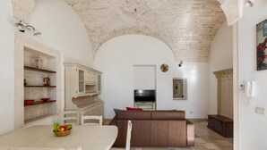 A spacious living area with a stone ceiling, a brown sofa, a dining table with chairs, and a TV on a stand. - 3189 Dimora Bellargo by Barbarhouse (Martina Franca)