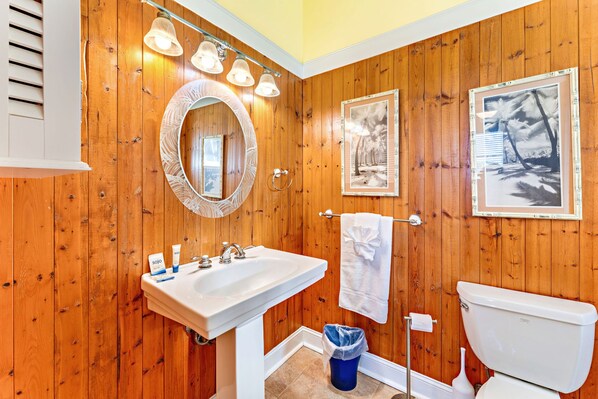 Un bagno con rivestimento in legno, un lavandino bianco, uno specchio e quadri appesi al muro.