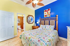 A bedroom with a bed, a wooden headboard, a nightstand with a lamp, a bathroom with a toilet and sink, and a ceiling fan. - Beachfront, Private home, dog friendly, heated pool, 4 BR (St. George Island)