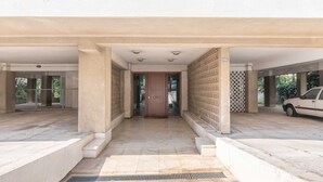 Un ingresso coperto con una porta centrale, un'auto parcheggiata a destra e un pavimento piastrellato.