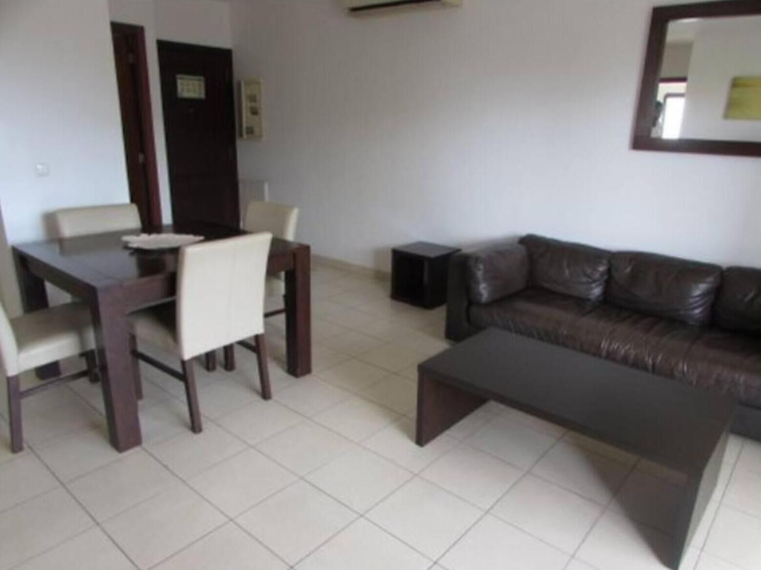 A living room with a dark brown leather sofa, a matching coffee table, and a dining area with a dark brown table and white chairs.