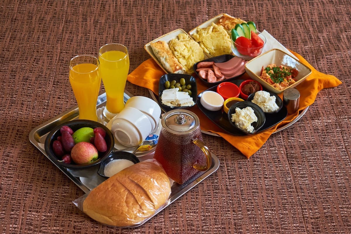 Un plateau de petit-déjeuner contenant divers aliments et boissons, notamment des œufs, des saucisses, du fromage et des fruits.