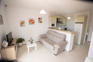 A compact living space with a sofa, a small table with a plant, a television, and a kitchenette area with a microwave and refrigerator.