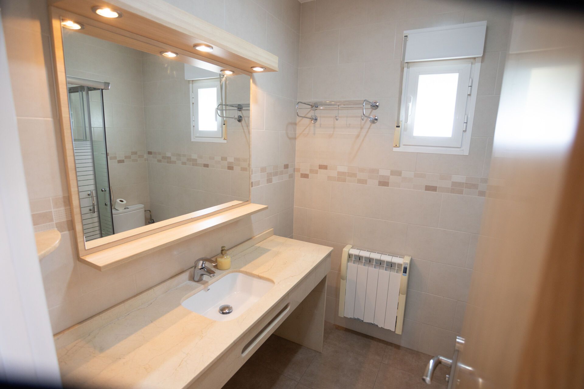 A bathroom with a sink, mirror, towel rack, and a window.