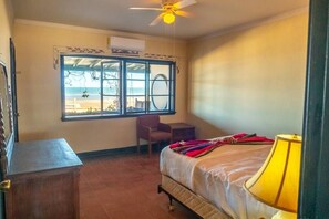 Quarto de hotel com cama, escrivaninha, cadeira, janela com vista e ventilador de teto.