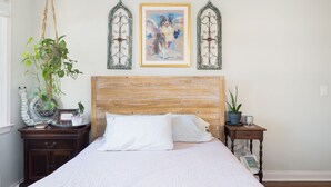 Ein Schlafzimmer mit einem hölzernen Kopfteil, einem großen Bett mit weißer Bettwäsche, einem Nachttisch mit einer Pflanze und einem gerahmten Gemälde über dem Bett.