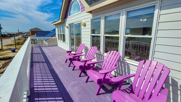 A covered deck with purple Adirondack chairs and a view of the ocean.