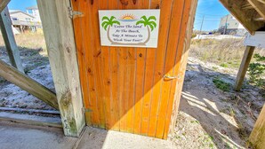 A wooden gate with a sign that reads "Leave The Sand At The Beach, Take A Minute To Wash Your Feet!"
