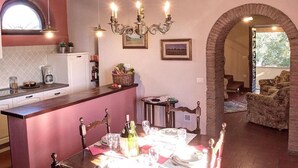 Una cucina accogliente con zona pranzo, caratterizzata da un soffitto in legno, un lampadario e un arco in mattoni che conduce a un soggiorno con un divano.