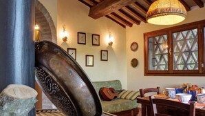 A rustic interior with exposed wooden beams, a stone fireplace, a green sofa, and a dining table with chairs. - The Olive  4+2 (Montescudaio)