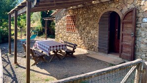 A rustic stone building with a wooden pergola, a checkered table, and a bench. - The Olive  4+2 (Montescudaio)
