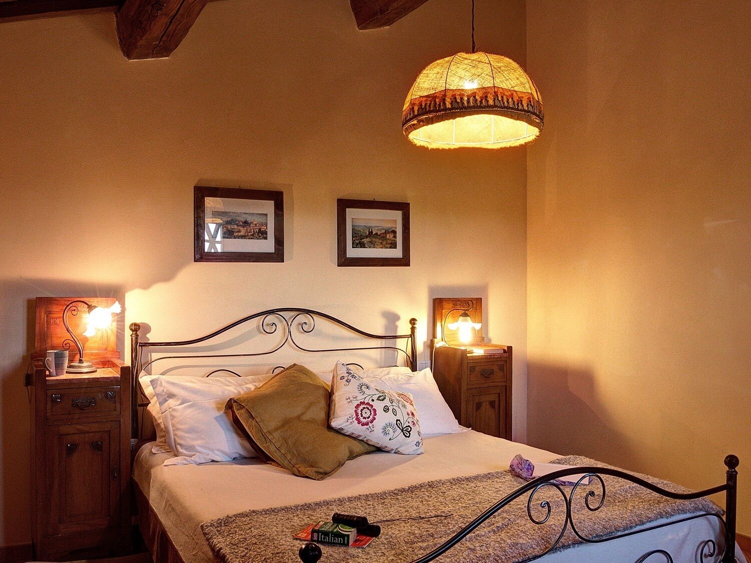 Un dormitorio con cama, dos mesitas de noche, una lámpara colgante y dos cuadros enmarcados en la pared.
