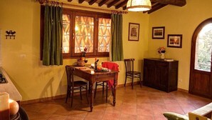 A dining area with a wooden table and chairs, a window with curtains, and a hanging light fixture. - La Capinere 2 2 (Montescudaio)
