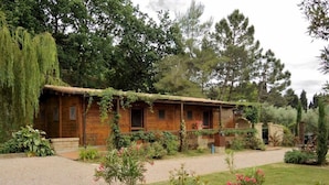 A rustic wooden cabin with a gravel driveway and a garden with various plants and flowers. - Lodge tent Fiordaliso 5 p. - Glamping, Nature, Tuscany 9 km from the sea (Montescudaio)