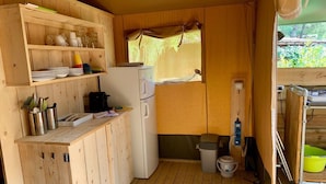 A compact kitchen with wooden cabinets, a refrigerator, a sink, and a window with a view of greenery. - Lodge tent Fiordaliso 5 p. - Glamping, Nature, Tuscany 9 km from the sea (Montescudaio)