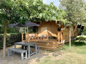 Une terrasse en bois avec une table et des bancs, un espace salon couvert et une petite construction dotée d’une cheminée.