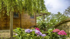 A wooden cabin with a garden in front, including hydrangeas and a pergola. - Lodge tent Fiordaliso 5 p. - Glamping, Nature, Tuscany 9 km from the sea (Montescudaio)