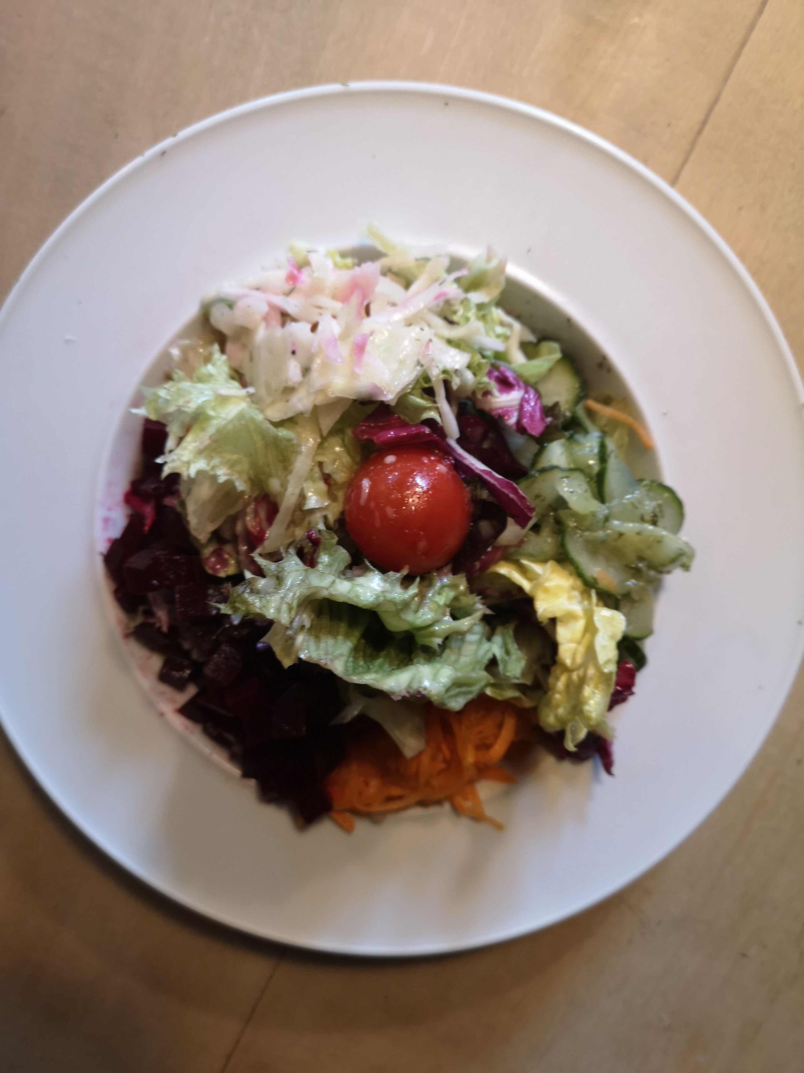 Une assiette blanche contenant une salade composée de laitue, de fromage râpé et d’une tomate cerise.