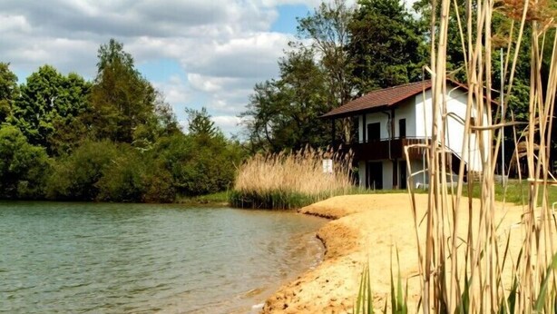 A lakeside property with a house, surrounded by dense greenery and tall grasses. - Brauereigasthof & Hotel Maierbräu (Altomunster)