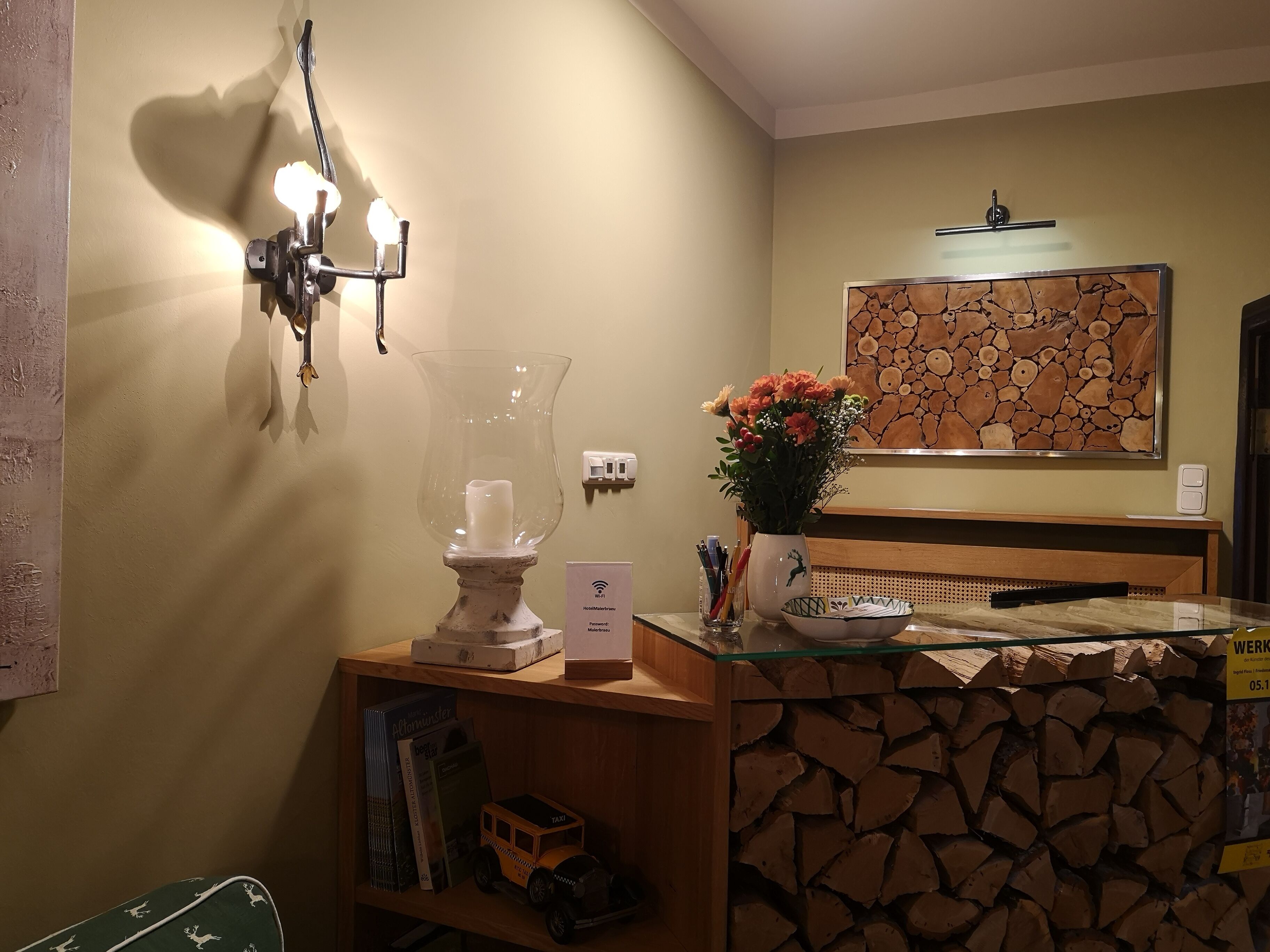 Un espace d’accueil d’hôtel avec un comptoir de réception en bois, un vase de fleurs, une horloge murale et une œuvre d’art encadrée au-dessus du comptoir.