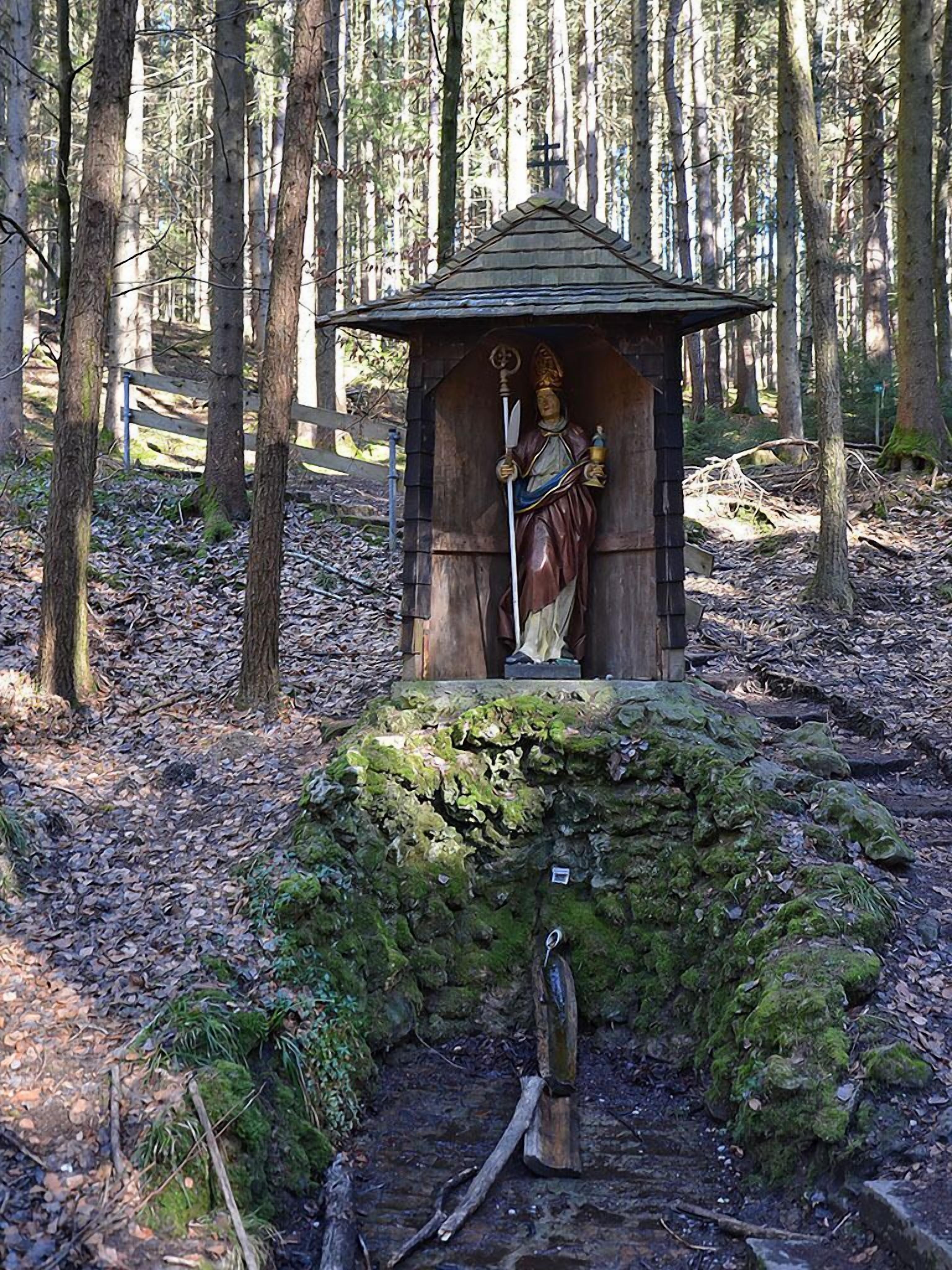 Una estructura de madera rústica con una estatua en su interior, rodeada de un bosque.