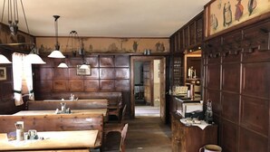 A rustic wooden interior with high wooden paneling, multiple wooden tables and benches, hanging pendant lights, and a bar area with shelves. - Brauereigasthof & Hotel Maierbräu (Altomunster)