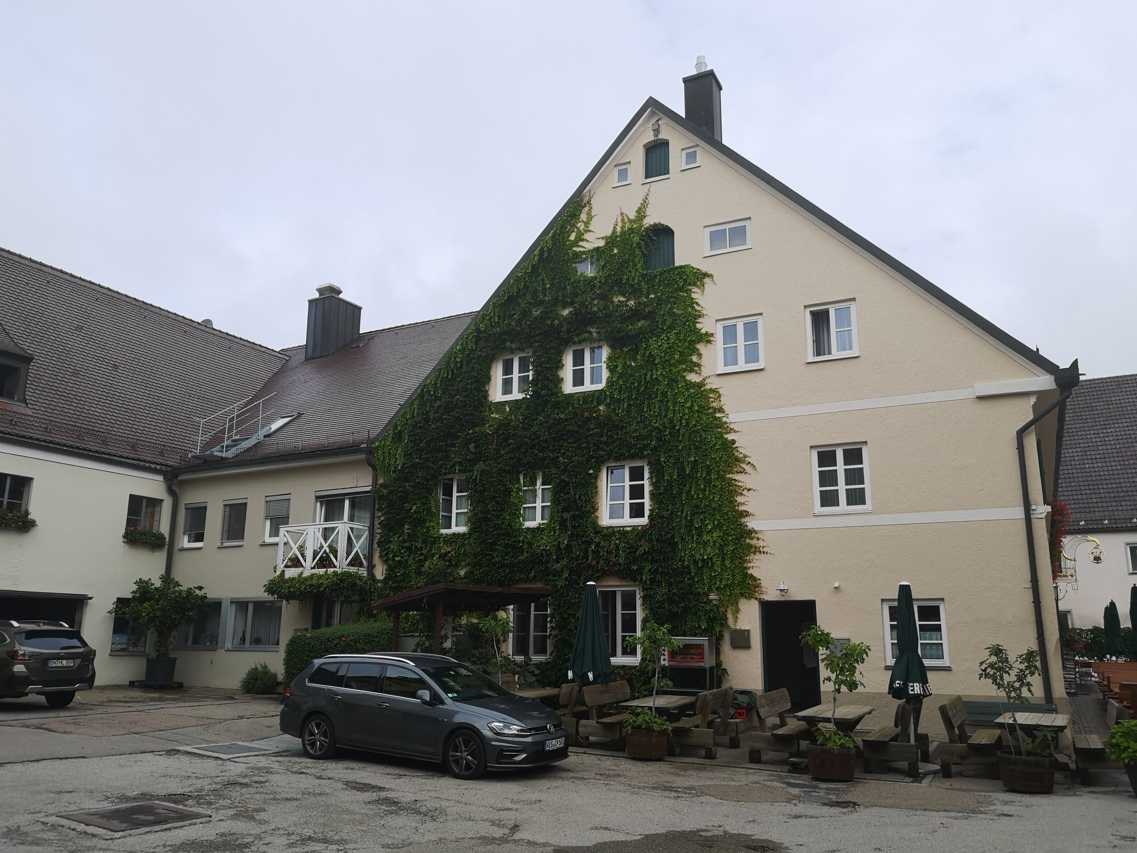 A building with a sloped roof, a car parked in front, and outdoor seating with umbrellas.