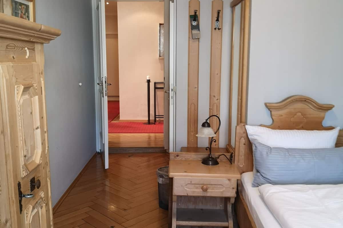 Ein Schlafzimmer mit einem hölzernen Bett, einem Nachttisch, einem Schreibtisch mit Lampe, einem Kleiderschrank und einem Holzboden mit Fischgrätmuster.