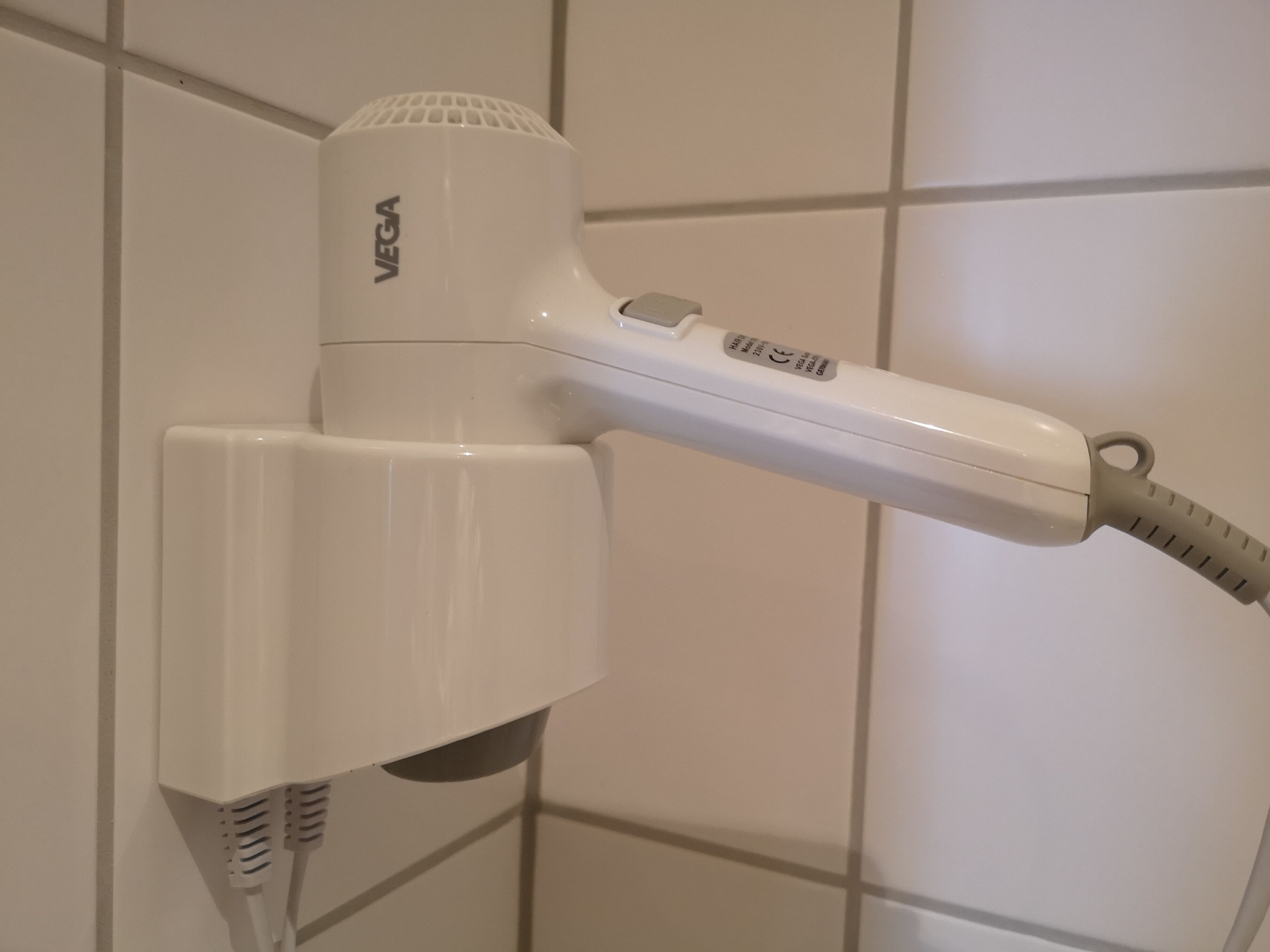 A white hair dryer mounted on a tiled wall.