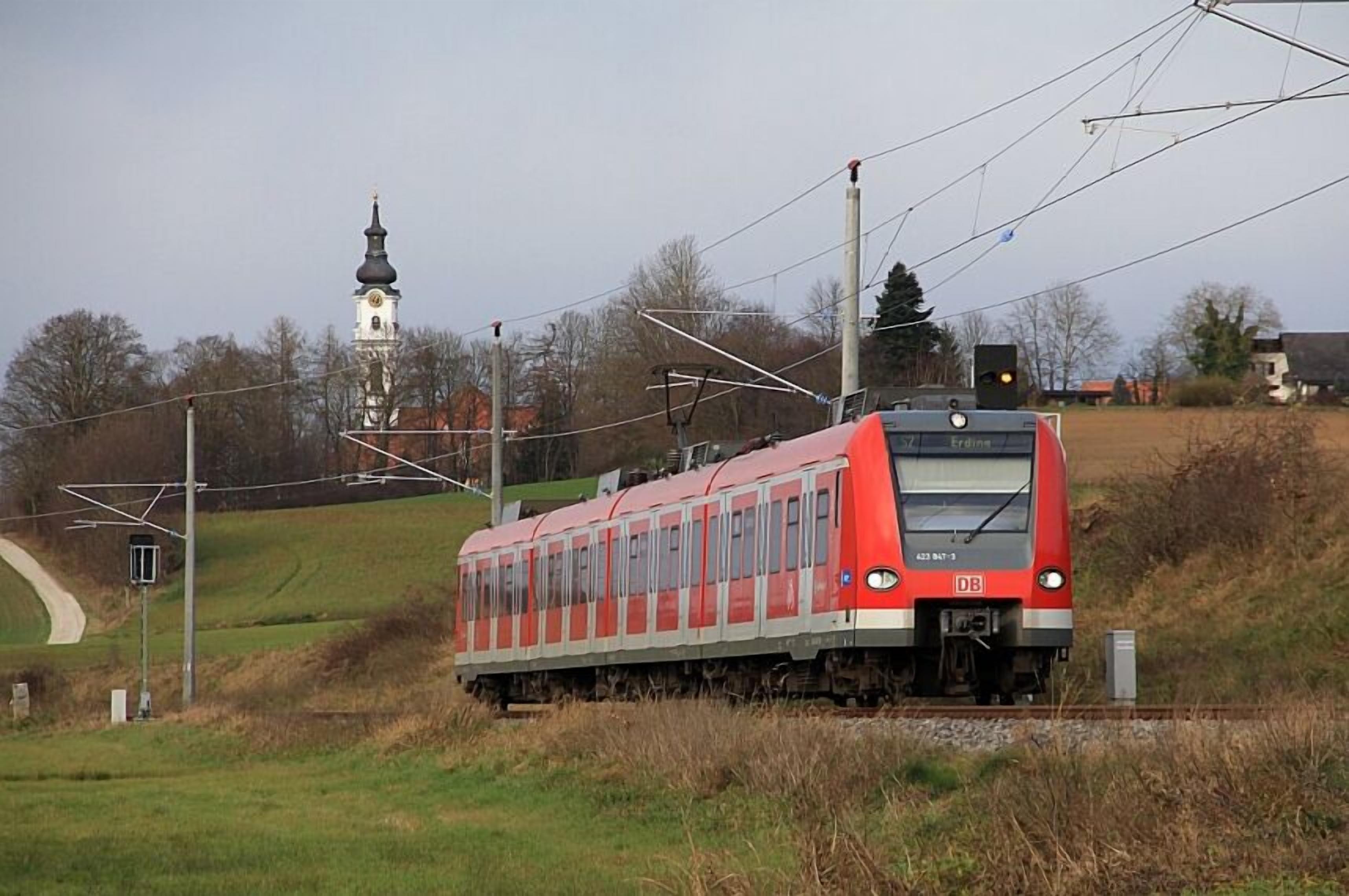 Een rode trein op rails, met een kerktoren op de achtergrond.