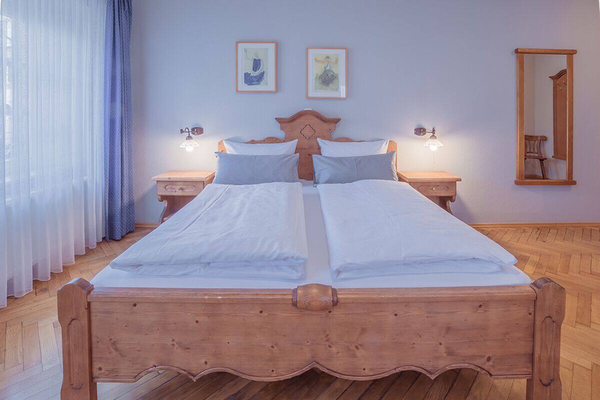 Ein Doppelbett mit Holzvorhang, zwei Nachttische mit Lampen und Kunstwerk an der Wand.