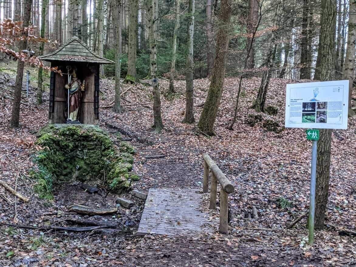 A forested area with a wooden structure, a wooden bridge, and a signpost.