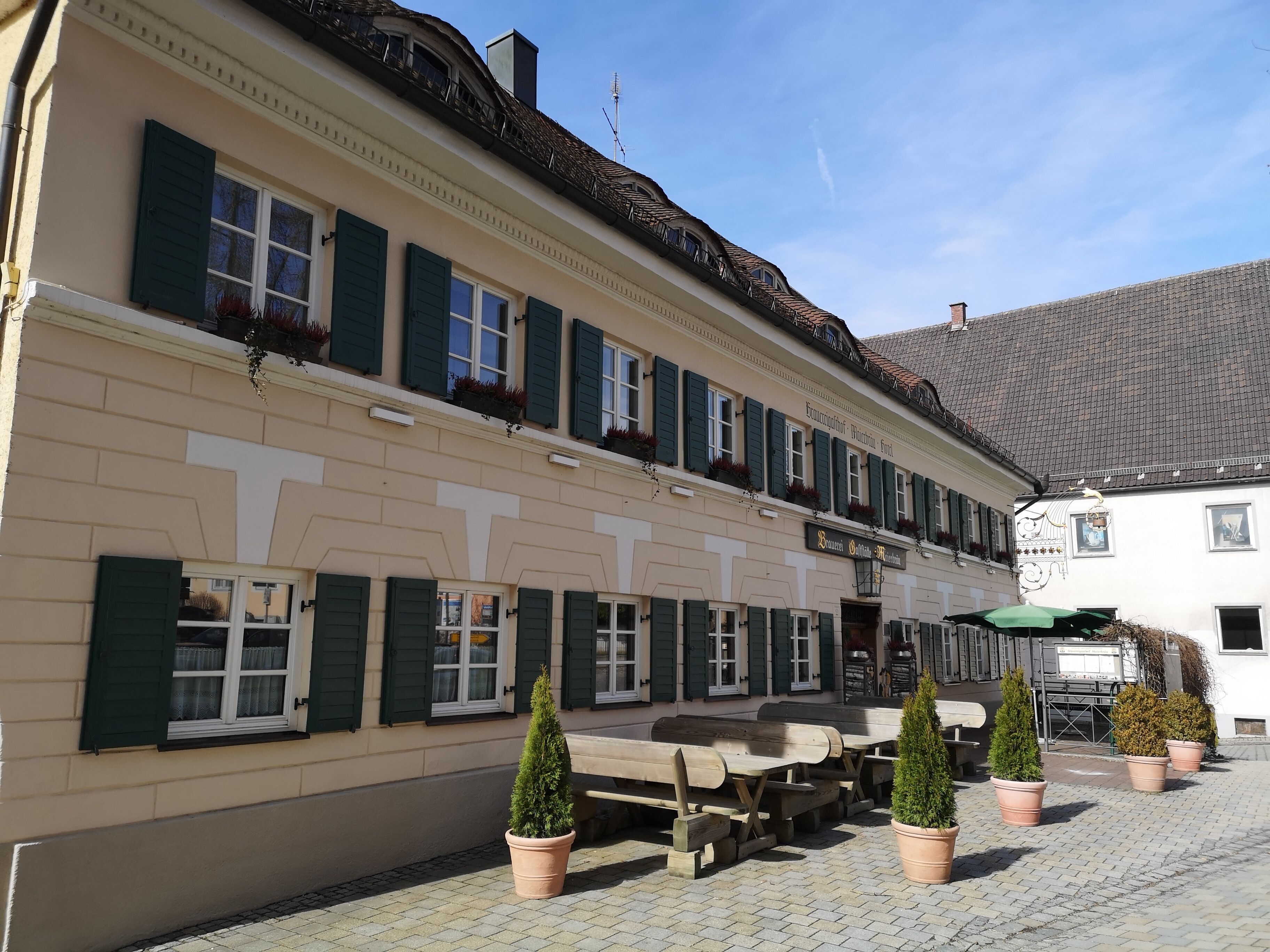 Een klassiek Europees gebouw met een rij ramen en luiken, terras en potplanten.