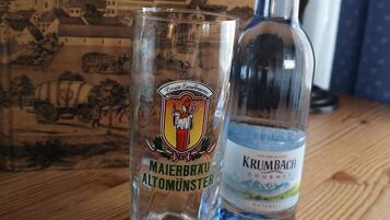 A glass and a bottle of Krumbach liquor on a wooden surface with a box labeled "Wilhelm Liebhart Altomünster" in the background.