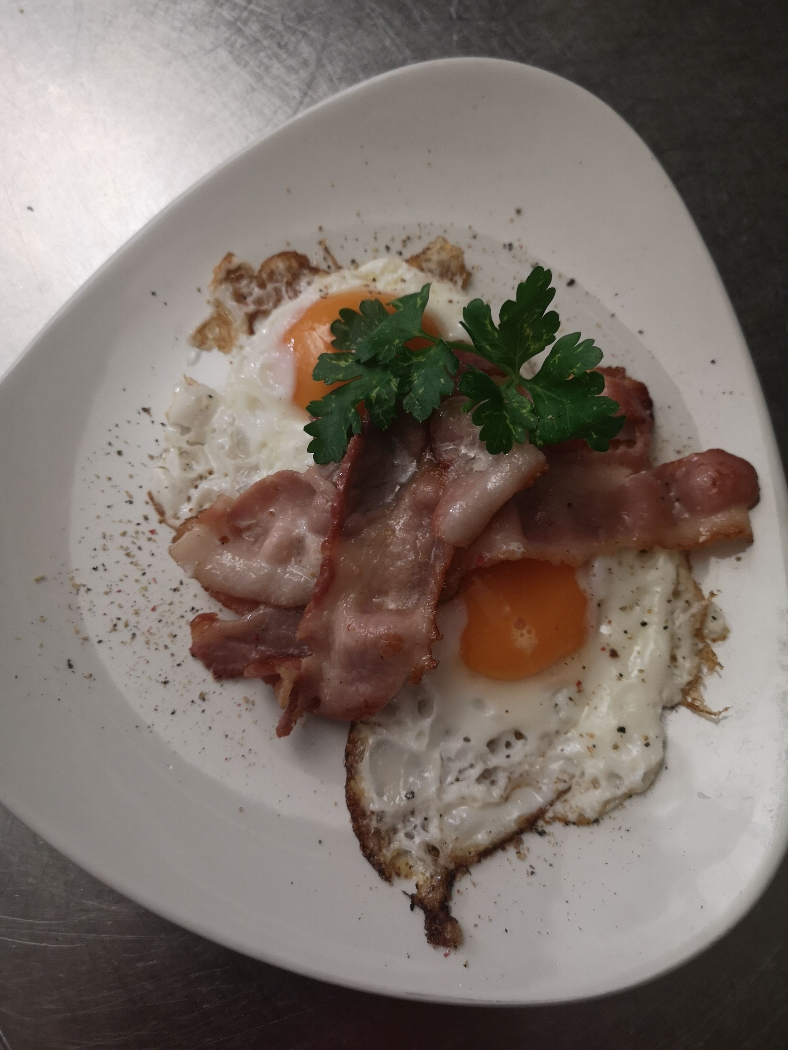 Um prato com dois ovos estrelados, fatias de bacon e um toque de salsa.