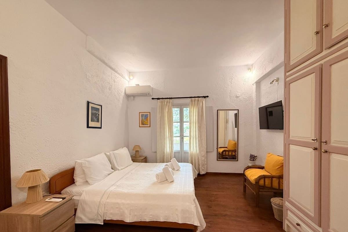 A bedroom with a bed, bedside table, lamp, and a chair.