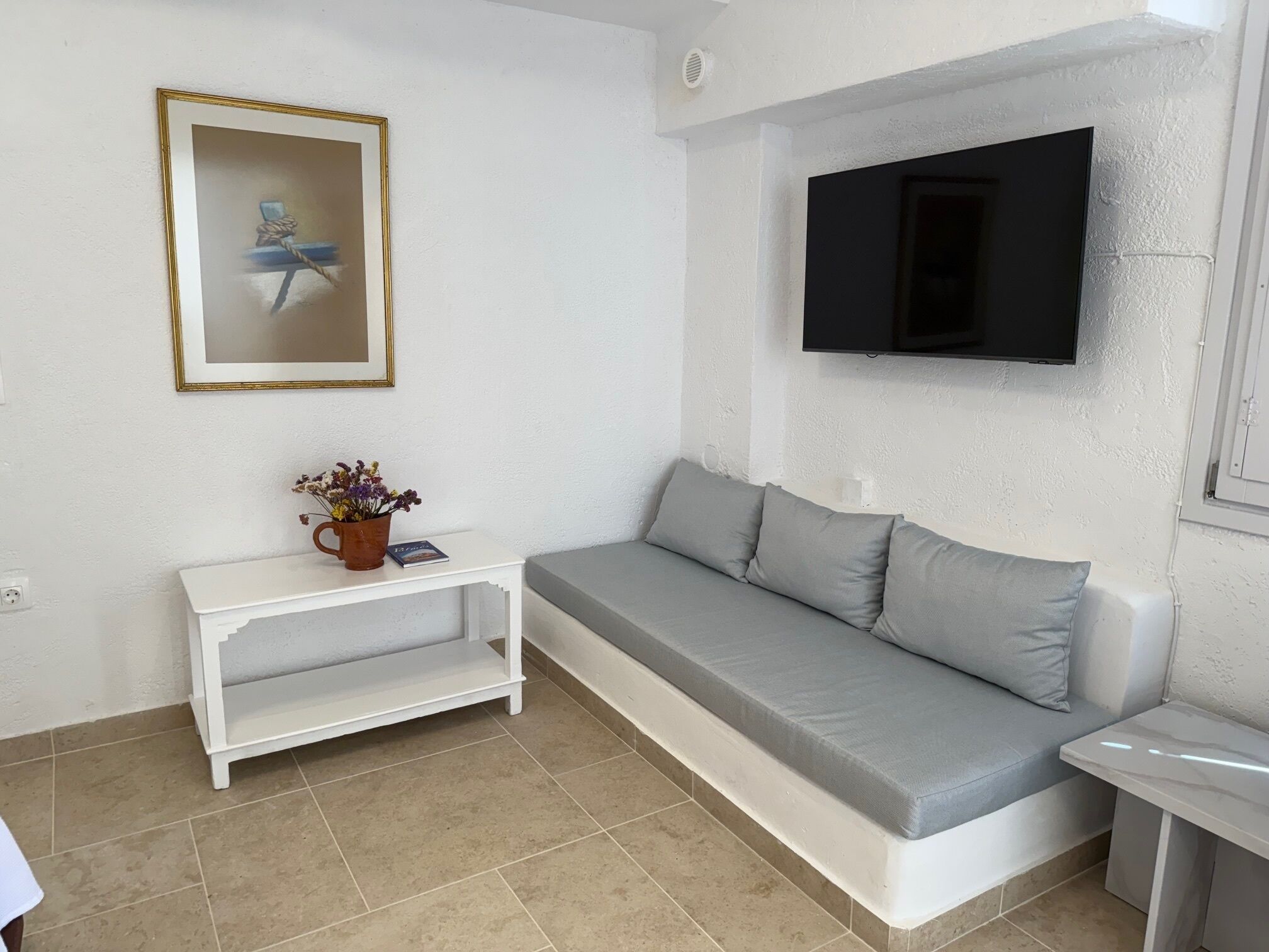 Una sala de estar con un sofá gris, una mesita auxiliar blanca, un cuadro enmarcado y un televisor de pantalla plana montado en la pared.