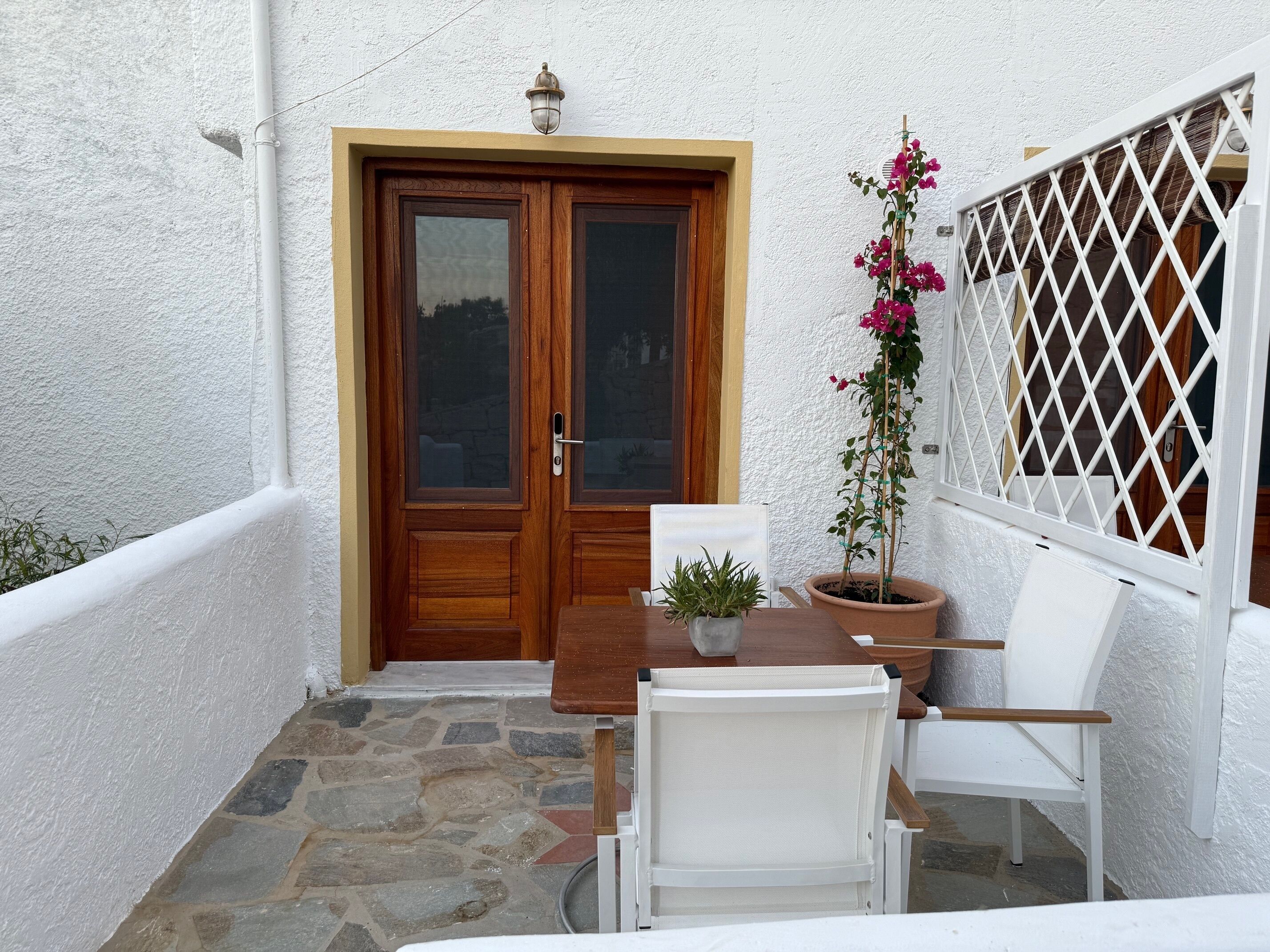Une petite terrasse extérieure avec une porte en bois, des murs blancs, une plante en pot et une chaise blanche.