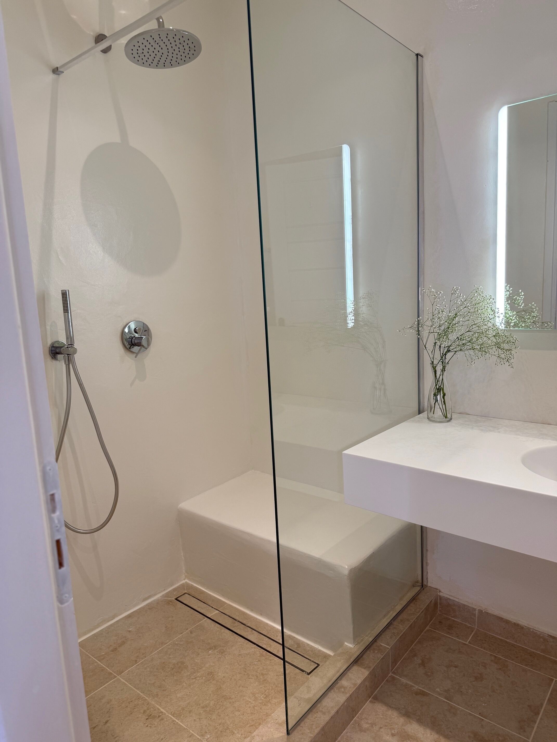 A modern bathroom with a glass shower enclosure, a white sink, and a mirror.