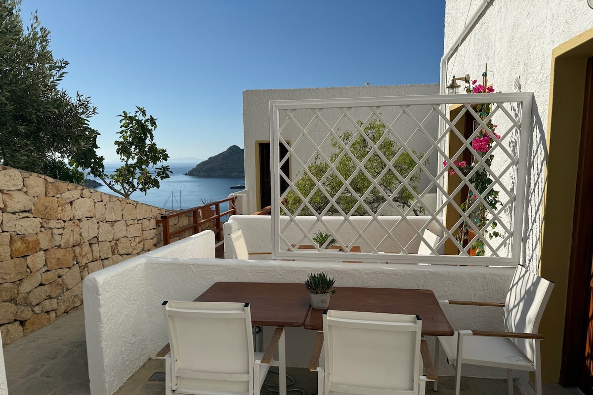 A terrace with a table and chairs, a stone wall, and a view of the sea.